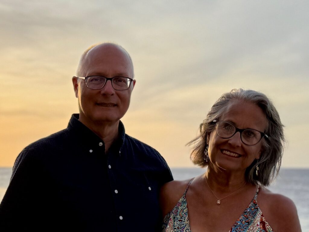 A man and woman at sunset on the Caribbean Sea. They are the authors of the website Retirement Unscripted,
