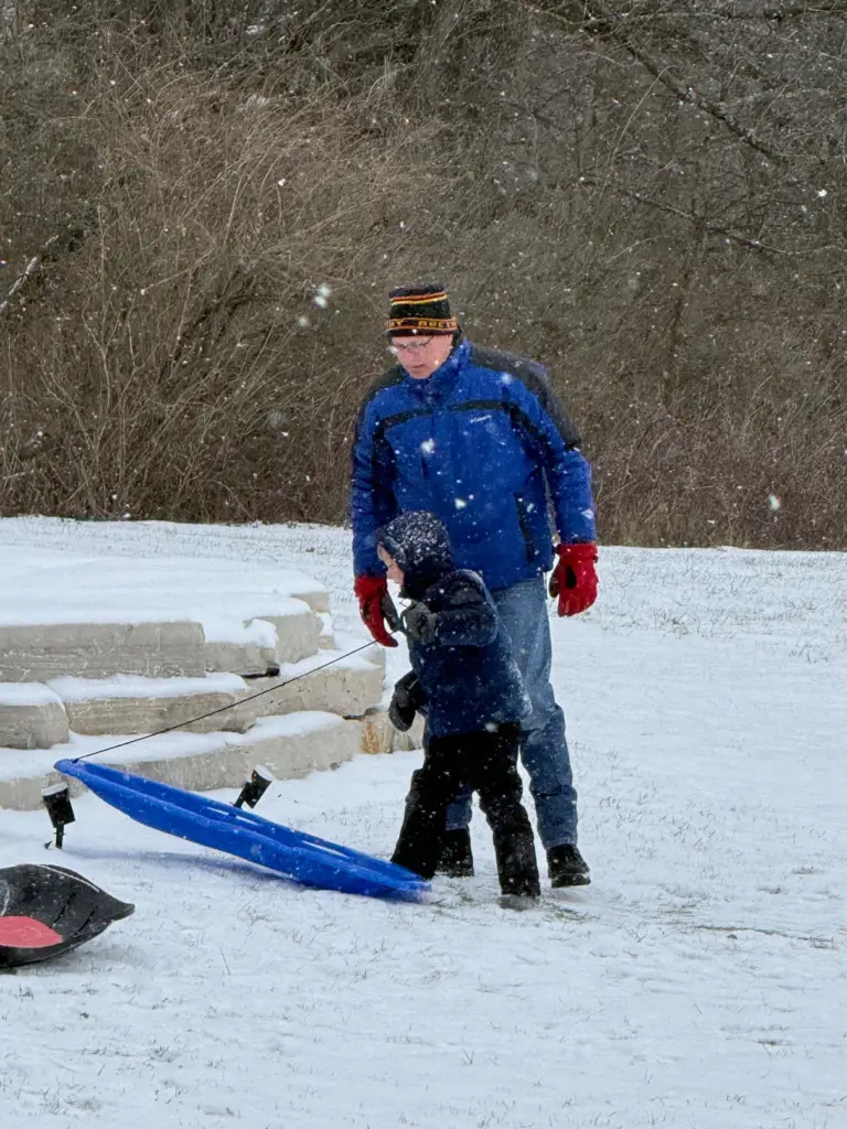 A man sledding with his grandson on a snowy day during an Illinois winter