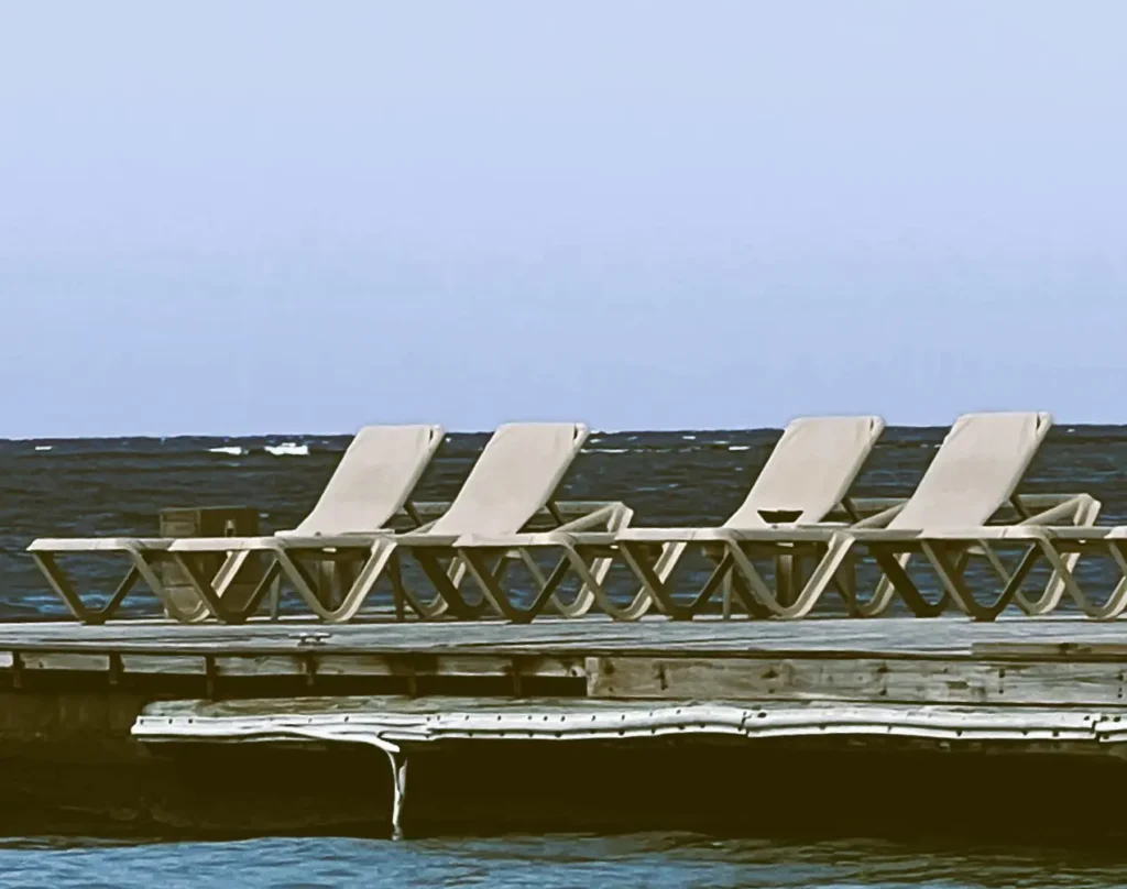 A row of empty sun loungers on a wooden dock beside the sea.